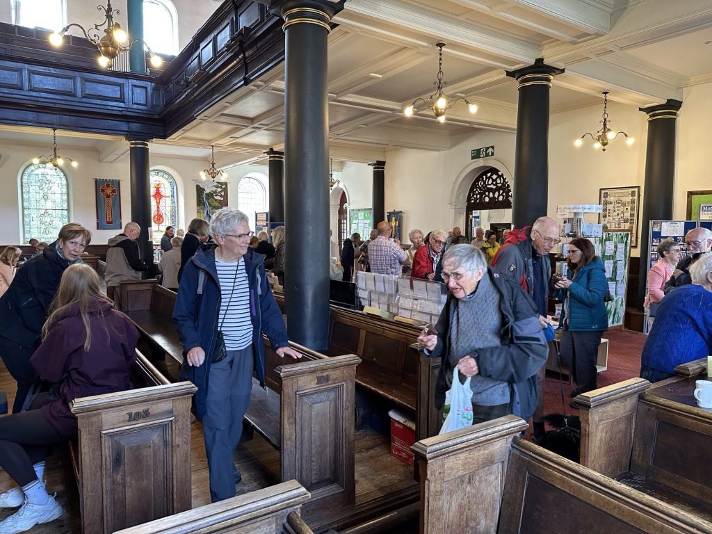 Zittende en staande, babbelende mensen in kerk. 
