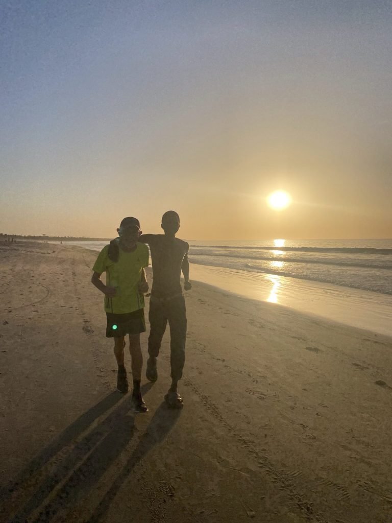 Jogger-toerist en lokale jogger bij zonsondergang op een strand in Gambia
