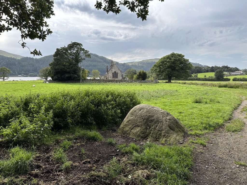 Groene weide, kerkje in de verte, meer en bergen. 