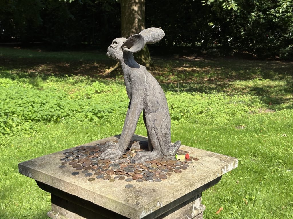 Gebeeldhouwd konijn op sokkel met muntstukjes. 