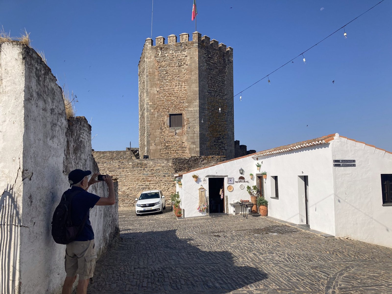 Toerist fotografeert vierkante toren van kasteel en wit huis in Monsaraz, Alentejo