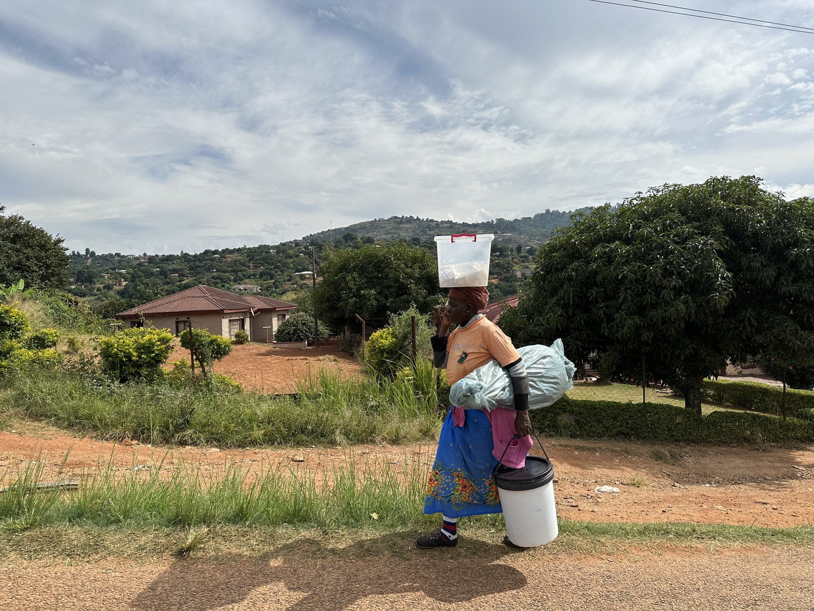 Afrikaanse vrouw met plastic emmer op hoofd.