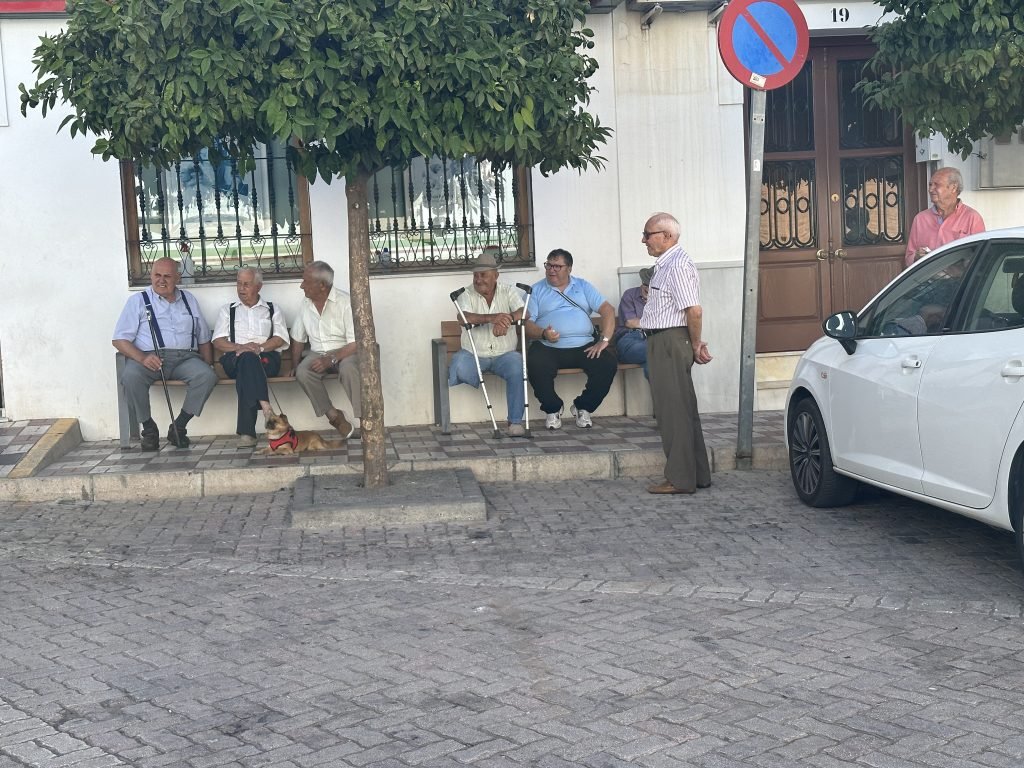 Oude mannen op bankjes voor witte gevel. 