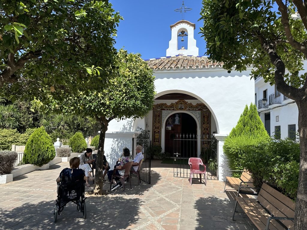 Ermita de San Antón: wit gebouwtje met ouderen op stoeltjes voor de ingang. 