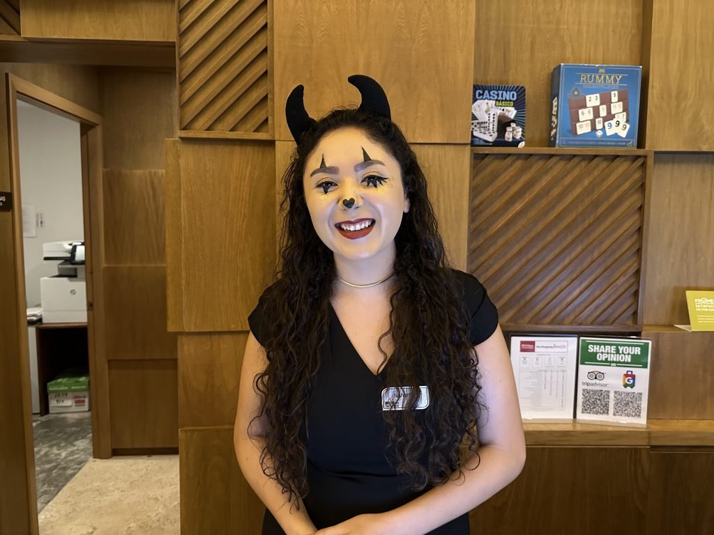 Hotel-receptioniste met duivel-horens en zwart hartje op punt van neus. 