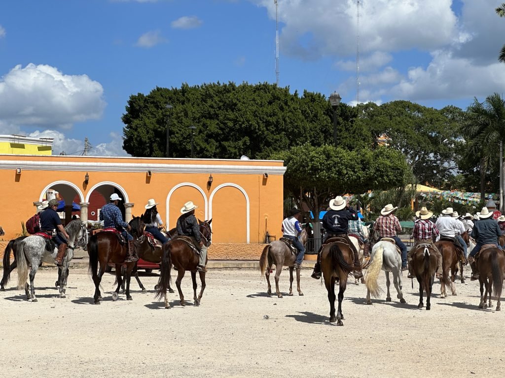 Cabalgata: ruiters voor okergeel gebouw. 