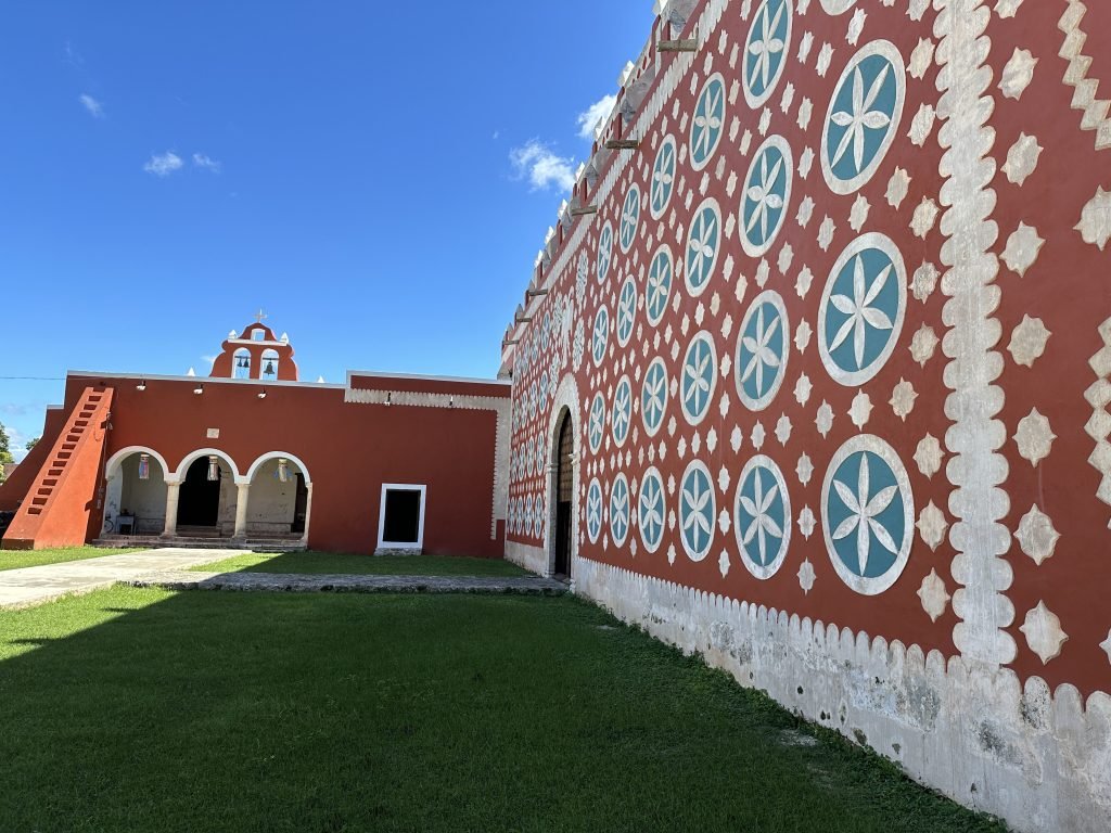 Zijmuur van de kerk met bruinrood gebouw achteraan. 