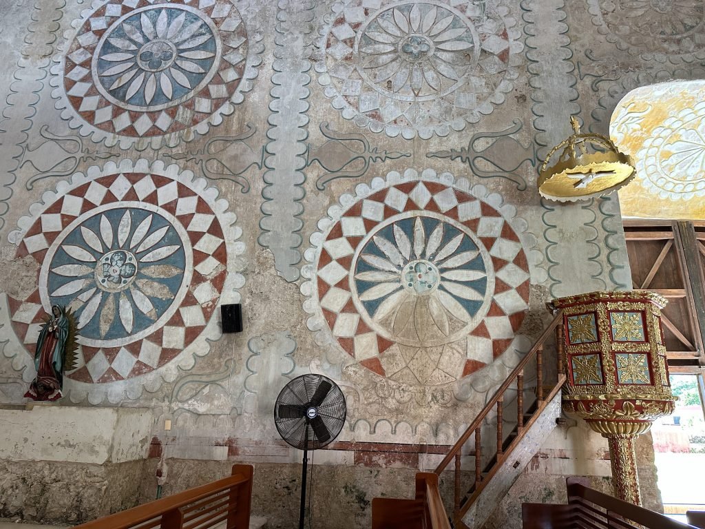 Close-up van de rozetten op een binnenmuur van de kerk met preekstoel rechts. 
