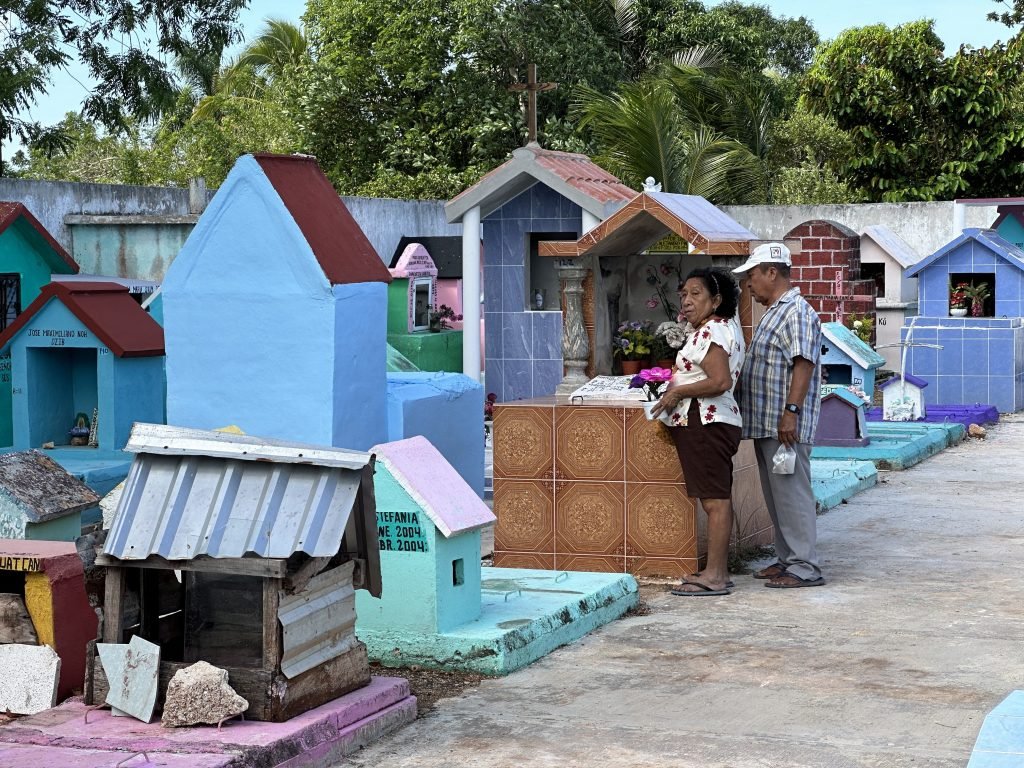 Mexicaans koppel met bloemen voor fel gekleurde grafkapel op kerkhof van Espita. 