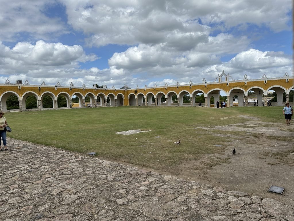 Groot, groen binnenplein met zicht op twee okergele zijden van het Convento de San Antonio de Padua